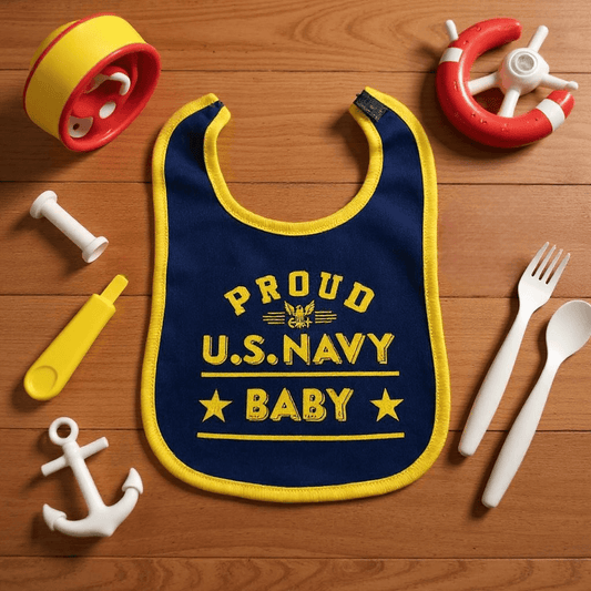 Proud U.S. Navy baby bib in navy color with yellow accents and print on a wooden surface.