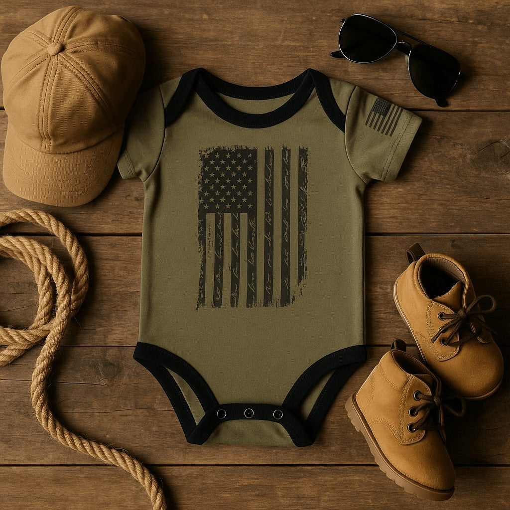 Patriotic Old Glory baby bodysuit with distressed American flag design on wood background, accessories styled.
