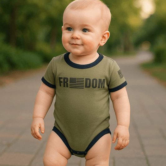 Baby in olive green Freedom Flag bodysuit with American flag design walking on a pathway outdoors.