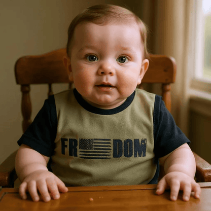 Baby wearing Freedom flag bib by Trooper Clothing, sitting in high chair with expressive face.